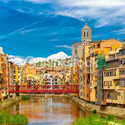 Colorful yellow and orange houses and Eiffel Bridge, Old fish stalls, reflected in water river Onyar, in Girona, Catalonia, Spain. Church of Sant Feliu and Saint Mary Cathedral at background.